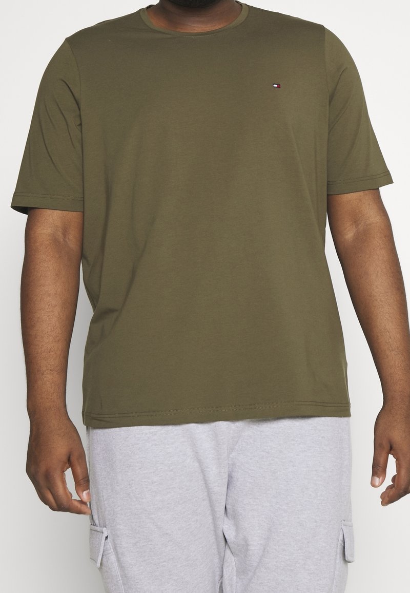 Muž v olivově zeleném tričku s krátkým rukávem a malým logem na hrudi a světle šedých cargo šortkách.