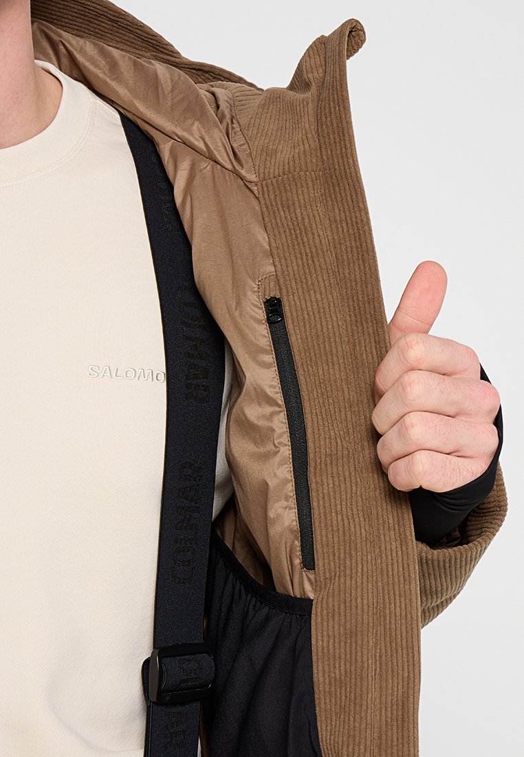 Braune Cordjacke mit Reißverschluss, schwarzem Innenfutter und verstellbaren schwarzen Riemen. Das Innenfutter ist glatt und leicht.