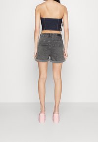 Top sin tirantes de denim con detalles de costura visibles, combinado con pantalones cortos grises de tiro alto, que presentan un dobladillo enrollado y dos bolsillos traseros.