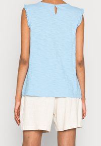Lysblå ærmeløs top med flæset skuldersøm og en nøglehulrygdetalje, parret med cremelavede linnedshorts.