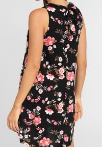 Schwarzes Blumenkleid mit ärmellosem Design, gebundenem Halsdetail und rosa-weißen Blumenspitzen auf dem Stoff.