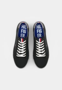 Černé plátěné tenisky s bílými tkaničkami, šedými detaily a modrou stélkou s nápisem "HILFIGER". Minimalistický design a kulatá špička.
