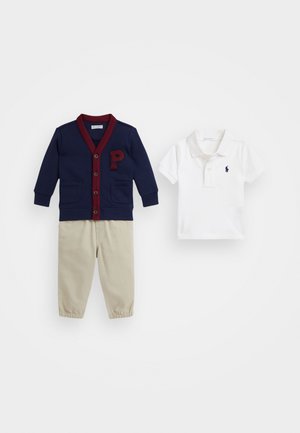 Cardigan bleumarin cu accente bordeaux și un patch cu litera "P", asociat cu o cămașă polo albă și pantaloni bej cu talie elastică.
