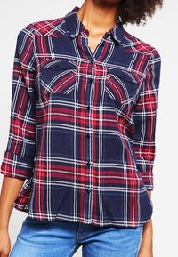 Camicia a quadri blu navy e rossa con bottoni, due tasche sul petto e maniche arrotolate, realizzata in tessuto leggero con una texture morbida.