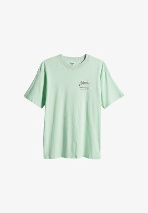 Maglietta in cotone verde menta con maniche corte, scollo rotondo e piccolo testo con logo sul davanti. Texture morbida, vestibilità rilassata, design casual.