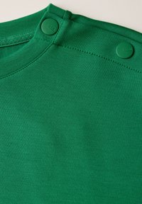 Grüne T-Shirt mit glatter Textur, ausgestattet mit einem runden Ausschnitt und zwei grünen Druckknöpfen an der Schulter. Einfaches, einfarbiges Design.