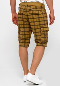 Kakigröna rutiga cargoshorts med flera fickor, avslappnad passform och en Calvin Klein-märkt midja, tillsammans med vita sneakers.