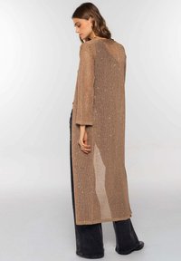 Cardigan largo y transparente en color beige, hecho de tejido de punto abierto con hilos metálicos, que presenta un ajuste holgado y un diseño simple y recto.