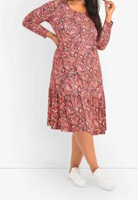 Vaaleanpunainen ja violetti paisley-kuvioinen mekko, jossa on pitkät hihat ja laaja helma, yhdistettynä valkoisiin tennareihin. Sileä pinta, pyöreä kaula-aukko.