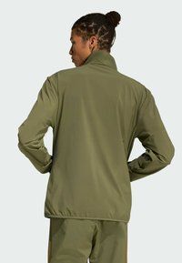 Olive green jacket with a high collar, sleek design, and long sleeves. Smooth texture with elastic cuffs and a rounded hem.