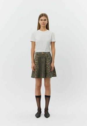 Valge lühikeste varrukatega t-särk sildiga, kantud põlvikupikkuse seelikuga, millel on tume leopardimuster, kombineeritud läbipaistvate mustade põlvikutega ja teravate kontsadega kingadega.