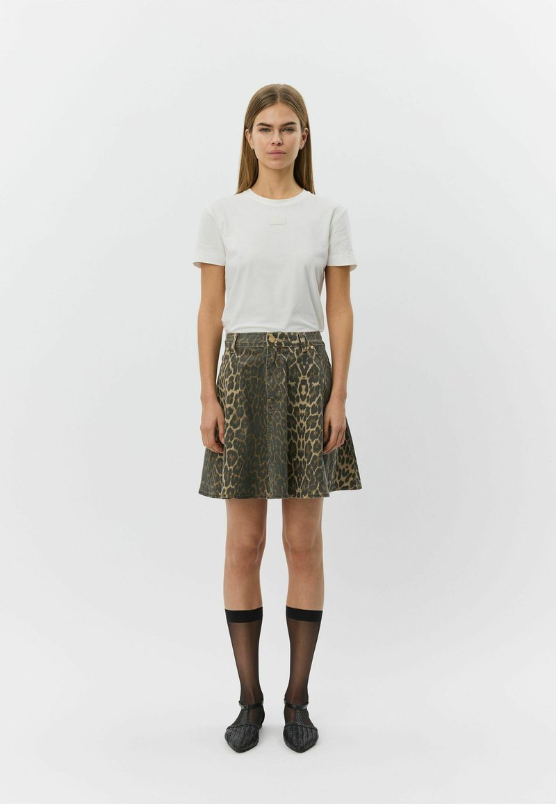 Camiseta blanca de manga corta con una etiqueta, combinada con una falda hasta la rodilla con estampado de leopardo oscuro, acompañada de calcetines negros transparentes hasta la rodilla y zapatos planos puntiagudos.