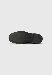 Black rubber shoe sole with embossed logo, patterned grooves, and a smooth texture; features a rounded toe and slight heel.