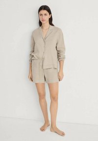 Linne tvådelat set bestående av en knapp-up skjorta med uppvikta ärmar och shorts med elastisk midja i mjuk beige färg. Enkel textur, avslappnad passform.