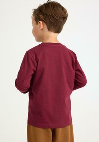 Langærmet mørkerød bomulds t-shirt med rund halsudskæring, glat tekstur og afslappet pasform, vist på et barn set fra ryggen.
