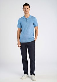 Jasnoniebieska dzianinowa koszulka polo z kołnierzykiem i krótkimi rękawami, zestawiona z granatowymi spodniami oraz białymi trampkami, stojąca na jednolitym tle.