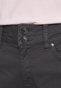 Šedé džíny mají dvojité zapínání, prošité pas a boční kapsu s minimalisticým designem.