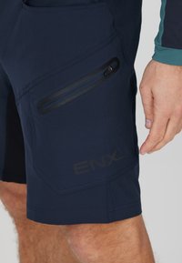Marineblaue Shorts aus leichtem Stoff mit einer seitlichen Reißverschlusstasche und „ENX“-Logo. Sie haben eine strukturierte Oberfläche und eine taillierte Passform.