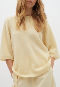 Šviesiai geltona per didelė megzta palaidinė, minkštas audinys, trumpomis rankovėmis ir įgaubtais rankogaliais. Yra apvalus apykaklė ir laisvas siluetas.