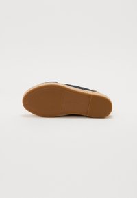 Suela de zapato azul marino con goma texturizada para agarre, que presenta un entresuelo de corcho claro y un borde curvado suave. Presencia mínima de marca.