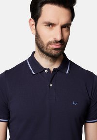 Granatowa koszulka polo z teksturowanej tkaniny, z zapięciem na dwa guziki, jasnoniebieską wąską kołnierzykiem i logo na lewej piersi.