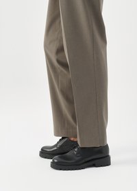 Scarpe in pelle nera con punta rotonda, design con lacci e suole robuste abbinate a pantaloni grigi a gamba larga.