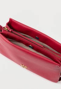 Punane nahast õla kott, millel on ülemine tõmblukk, kuldse tooni detailid ja sile tekstuur, lisaks sisemine tõmbluku tasku.