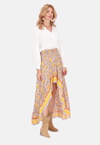 Weiße Langarmbluse, Maxi-Rock mit Blumenmuster in Gelb- und Orangetönen und beigefarbene Knöchelstiefel mit Lochmuster.