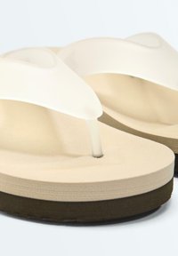 Sandales tongs beiges avec semelles épaisses marron foncé et larges brides translucides sur fond blanc.