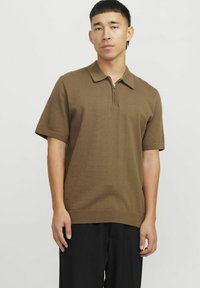 Polo shirt marron à manches courtes avec un col zippé, texture côtelée et coupe décontractée, accompagné d'un pantalon noir.