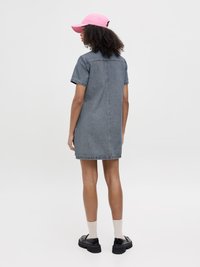 Denimkjole med korte ermer, midt på låret, steinvasket finish, kombinert med en rosa caps og svarte klumpete sko.