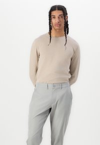 Lyse beige sweater lavet af blødt stof, parret med lyse grå bukser med knaplukning og lige ben. Enkel og nedtonet.
