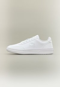 Hvite tennissko med en glatt syntetisk overdel, rund tå, snøring og et enkelt logo. Har en flat gummisåle for stabilitet.