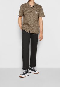 Koszula z krótkim rękawem w panterkę w odcieniach brązu i czerni, zestawiona z czarnymi spodniami i czarnymi trampkami z białymi i brązowymi akcentami.