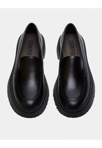 Chaussures slip-on noires en cuir lisse avec un bout rond, semelle en caoutchouc épaisse et design minimaliste. L'intérieur comporte le logo de la marque.