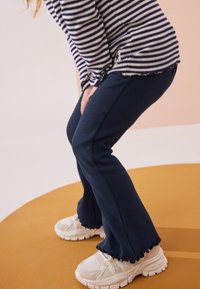 Top de manga larga a rayas con dobladillo redondeado, combinado con pantalones acampanados de canalé en azul marino y zapatillas deportivas blancas con detalles texturizados.