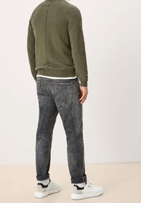 Olivgrüner Strickpullover mit rundem Ausschnitt, kombiniert mit dunkelgrauen Jeans. Weiße Sneakers mit schwarzen und grauen Akzenten.