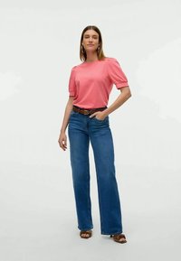 Rosa, t-skjorte med kort erm og puffede ermer, kombinert med blå, flagrende jeans og brunt belte. Brune sandaler med teksturerte stropper.