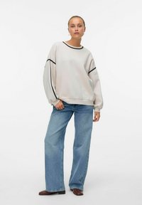 Lysegrå genser med svarte detaljer, løs passform, senkede skuldre, ribbestrikkede mansjetter, kombinert med høytlivs blå jeans og brune sko.