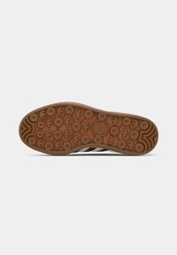 Brown rubber outsole with circular grip pattern; three black stripes design; smooth, slightly raised edges and logo detail at the center.