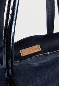 Τσάντα ώμου από καμβά σε ναυτικό μπλε με λαβές διακοσμημένες με παγιέτες, κλείσιμο με φερμουάρ και καφέ δερμάτινη ετικέτα που αναγράφει "LE CABAS VANESSA BRUNO MADE IN FRANCE".