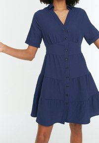 Marinblå skjortklänning med korta ärmar, knappar framtill, lagerdesign, texturerad tyg och rundad fåll.
