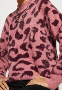 Fuzzy rosa tröja med mörklila abstrakta leopardmönster, rund hals och långa ärmar. Inkluderar ett silverkedjehalsband som accent.