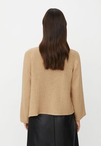 Beiger Strickpullover mit weiten Ärmeln und lockerem Sitz, kombiniert mit einem schwarzen Lederminirock. Die Textur wirkt weich und gemütlich.