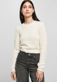 Weißer, flauschiger Pullover mit Rundhalsausschnitt und langen Ärmeln, kombiniert mit dunklen, hochgeschnittenen Jeans. Weicher Stoff und lässige Passform.