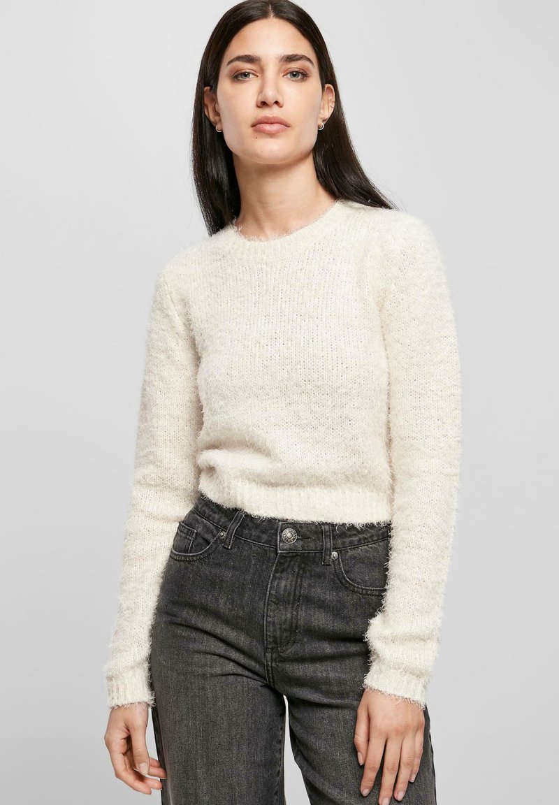 Pullover bianco e soffice con scollatura rotonda e maniche lunghe, abbinato a jeans scuri a vita alta. Tessuto morbido e vestibilità comoda.