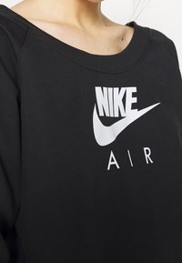 Närbild av en person som bär en svart sweatshirt med en vit Nike Air-logotyp över bröstet.