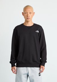 Swartrykt svart sweatshirt laget av bomullsmiks, med rund hals, ribbede mansjetter og en liten hvit logo på øverste venstre bryst.