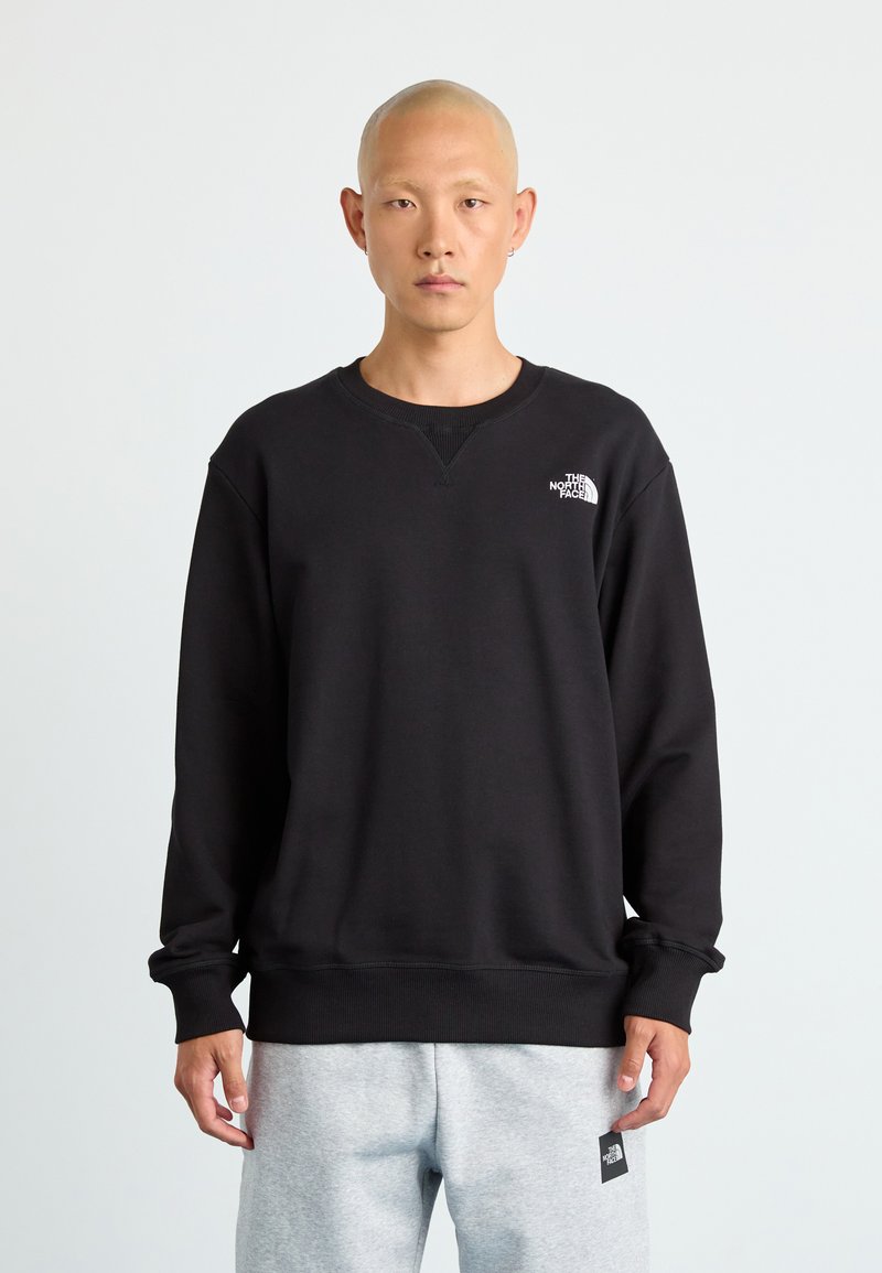 Swartrykt svart sweatshirt laget av bomullsmiks, med rund hals, ribbede mansjetter og en liten hvit logo på øverste venstre bryst.