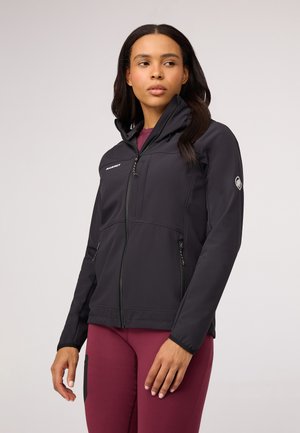 Svart softshell-jakke med glidelås foran, høy krage og to sidelommer. Har et logo på brystet og en teksturert finish.